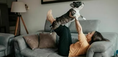 En dame ligger i en sofa og leker med en hund. Foto