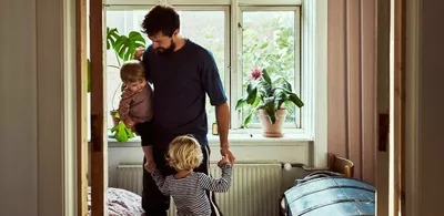 En far står på et rom med sine to barn. Foto