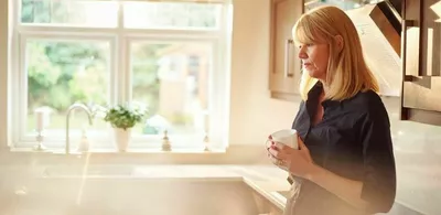 En dame står på et kjøkken og holder en kaffekopp. Foto