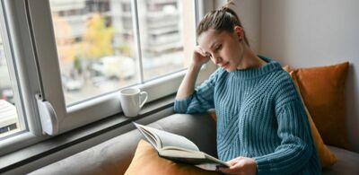 En dame sitter i en sofa og leser en bok. Foto