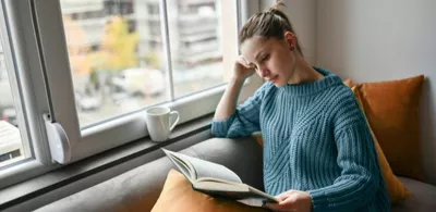 En dame sitter i en sofa og leser en bok. Foto